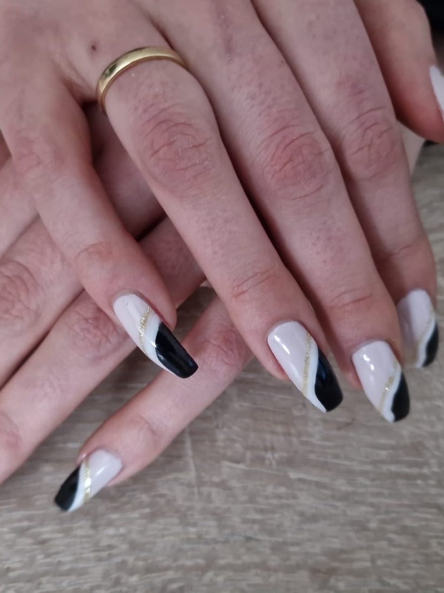Nahaufnahme von schwarz-weißen Gel-Nägeln in Sargform mit feiner goldener Diagonallinie auf Holzuntergrund
